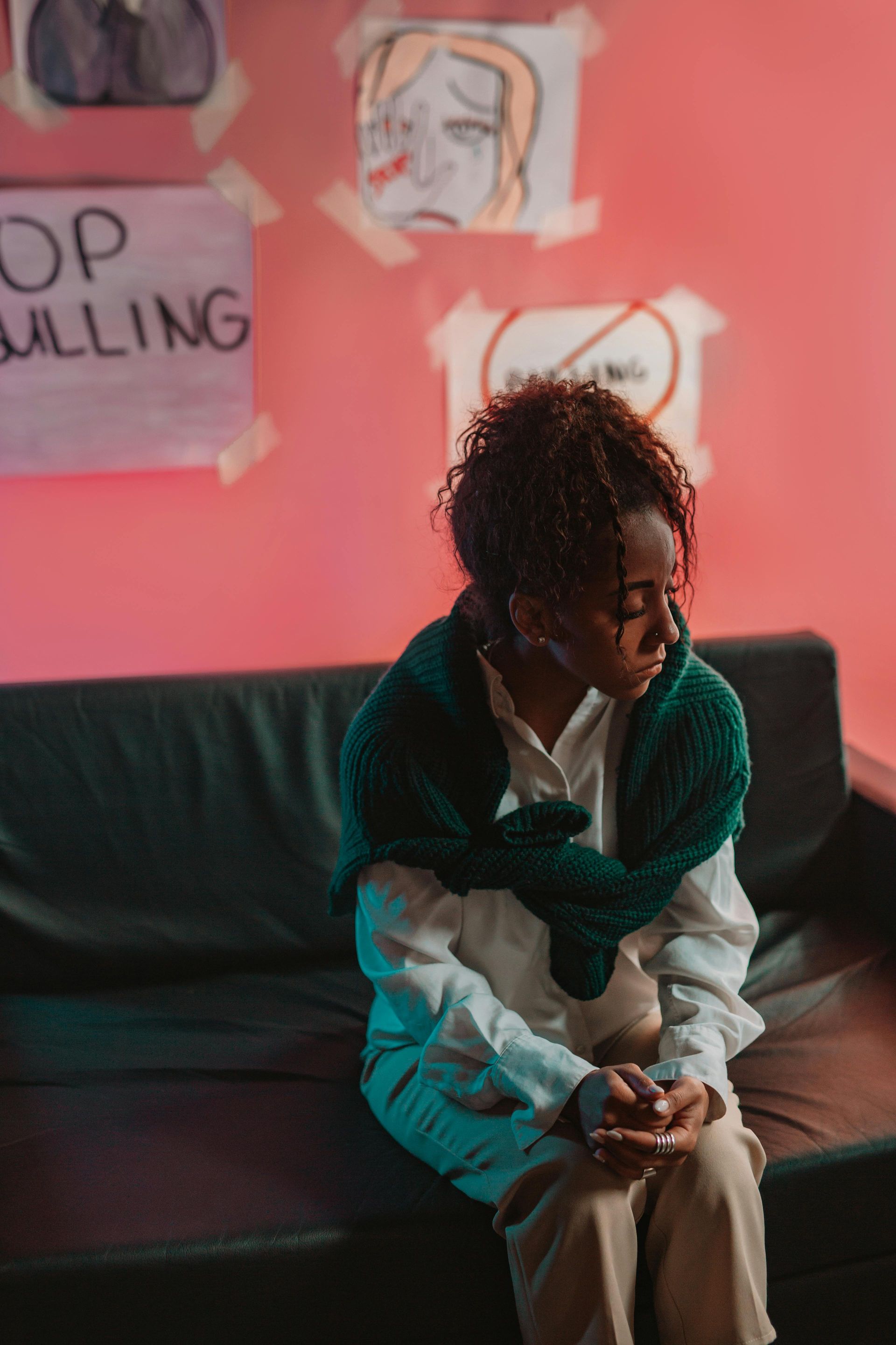 Person sitting on a couch, looking down, with a “STOP BULLYING” sign on the pink wall behind them.