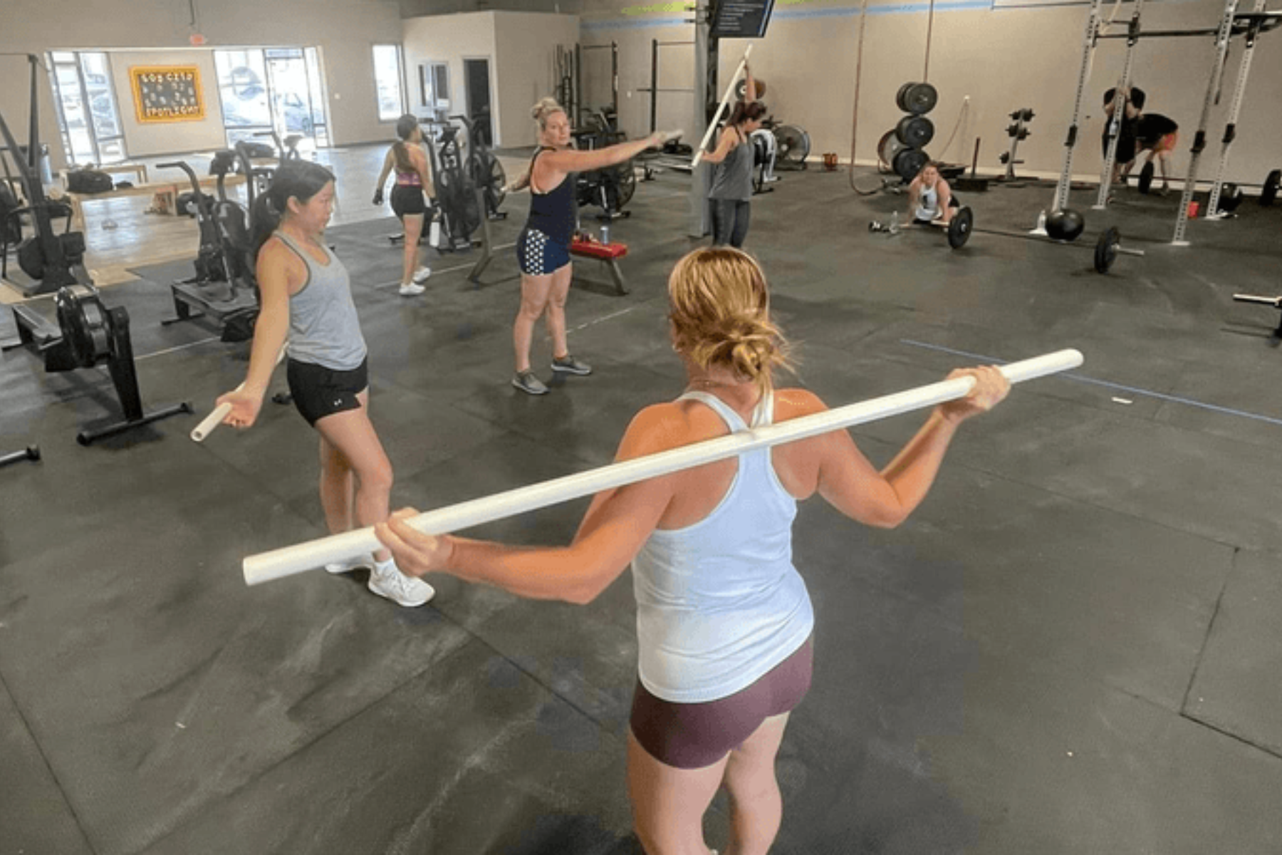 A group of women are standing in a gym holding a barbell.