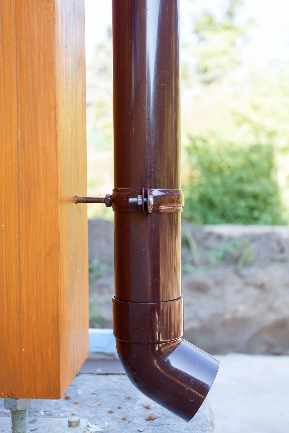 Tubo di scarico marrone fissato a una parete di legno, che termina con un gomito curvo vicino al terreno.