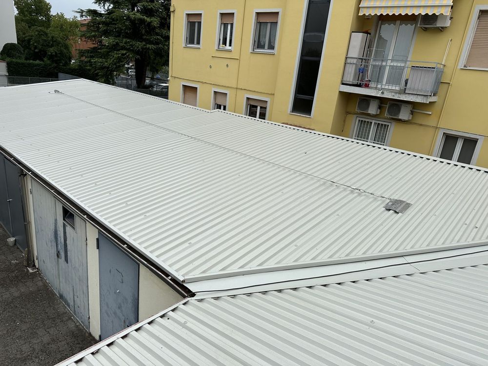 Tetto in lamiera ondulata bianca sopra gli edifici dei garage accanto a un condominio giallo.