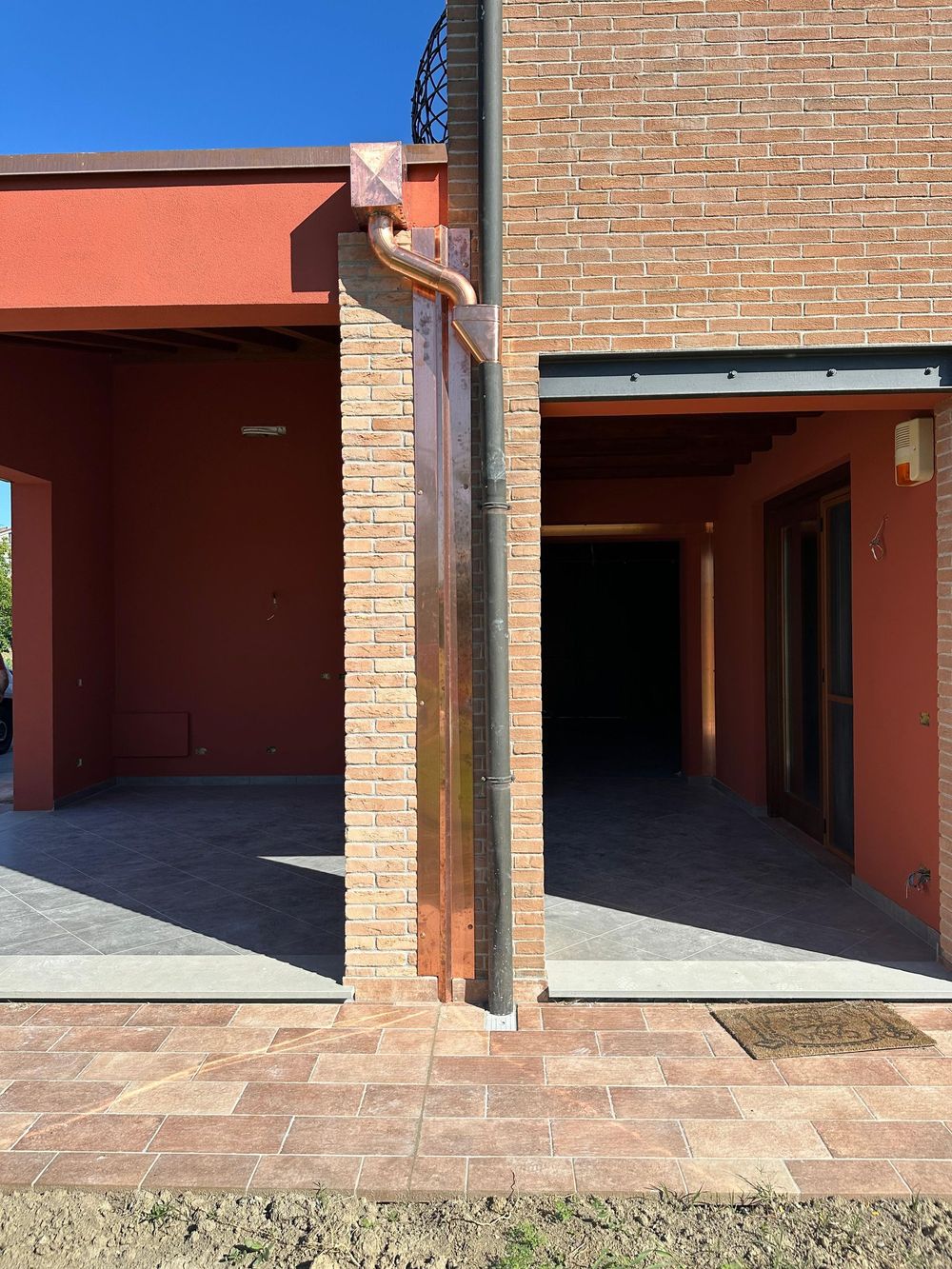 Primo piano di un tubo di scarico di una grondaia sotto la grondaia di un tetto di un edificio, con il rivestimento arancione visibile al di sotto.