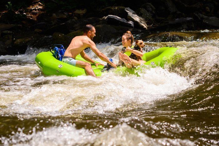 A man and a woman are floating down a river in a green raft.