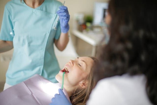 Woman in dental chair, mouth open, dentist and assistant attending.