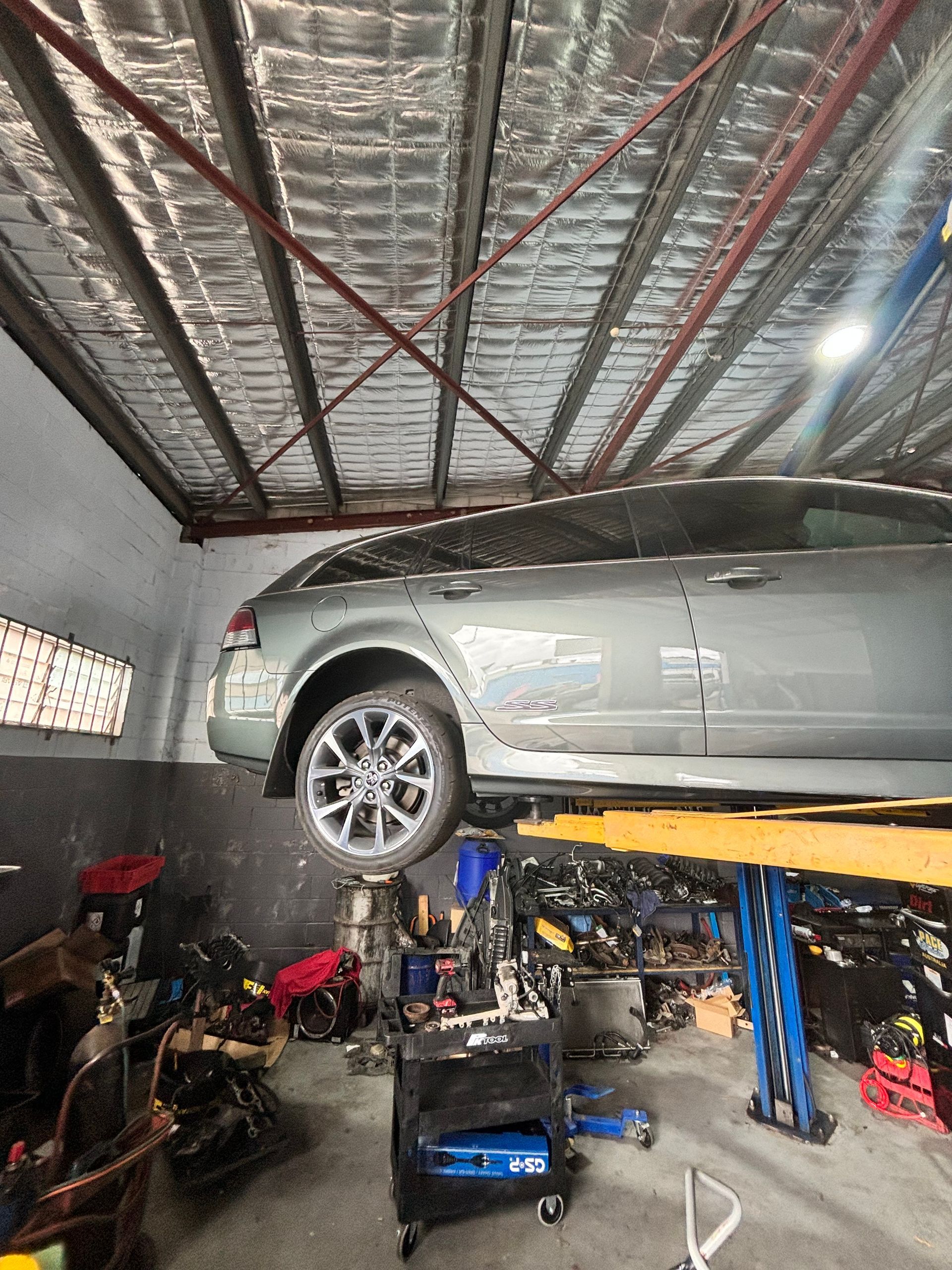 Silver Car Raised on a Lift in a Cluttered Auto Repair — Total Auto Service In Caloundra West, QLD