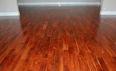 Polished, warm-toned reddish-brown hardwood flooring extending from the foreground into a room with light-colored walls.
