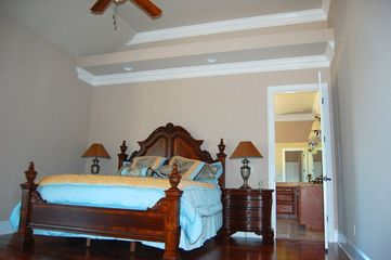 A bedroom with a large dark wood sleigh bed, blue bedding, two matching nightstands with lamps, and an open bathroom.