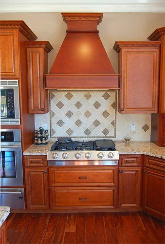 A kitchen stove area featuring wood cabinetry, a decorative tile backsplash, and a large custom wood range hood.