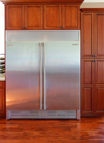A large stainless steel double-door refrigerator built into custom cherry wood cabinetry in a kitchen.