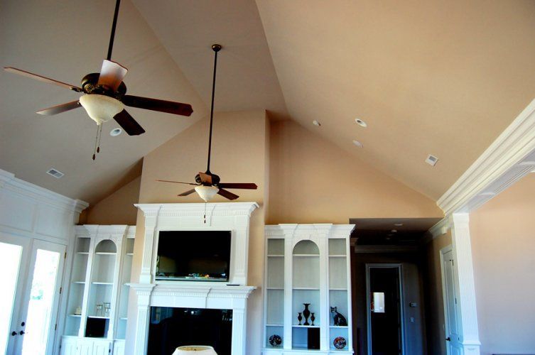 Living room with vaulted beige ceilings, two ceiling fans, and white built-in bookshelves flanking a fireplace.