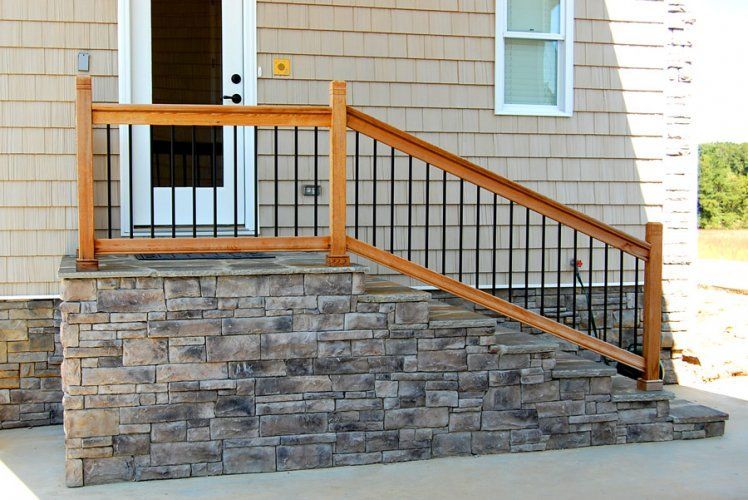 Exterior view of stone steps with wooden railings leading to a white door on a house with beige shingle siding.