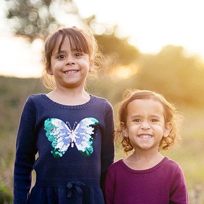 Two girls stand in a field with sunlight.