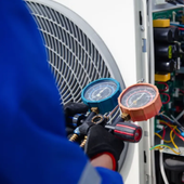 Technician using gauges on an HVAC unit with blue and orange dials, wires visible in the background