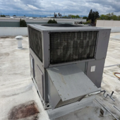 Rooftop HVAC unit with open access panel on a flat white roof, city skyline in the background