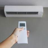 Hand holding an air conditioner remote pointed at a wall-mounted AC unit