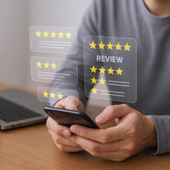 Person holding a smartphone with floating star review ratings and “REVIEW” icons above a desk