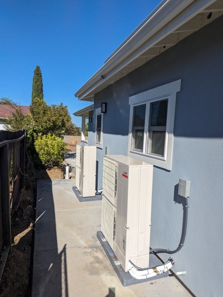 Side yard with a blue house exterior, narrow concrete walkway, and utility equipment beside a fence.