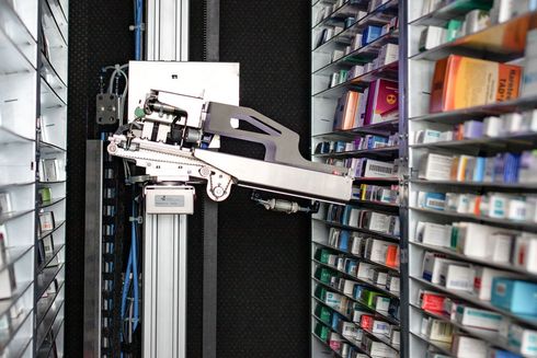Ein automatisierter Apothekenroboter entnimmt Medikamente aus einem mit Regalen gefüllten Lagerbehälter.