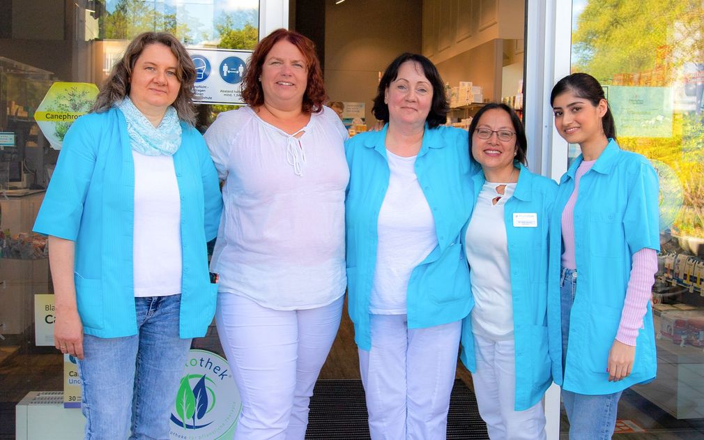 Fünf Personen in türkisfarbenen Jacken und weißen Hemden stehen vor einem Geschäft mit einem Logo an der Tür.