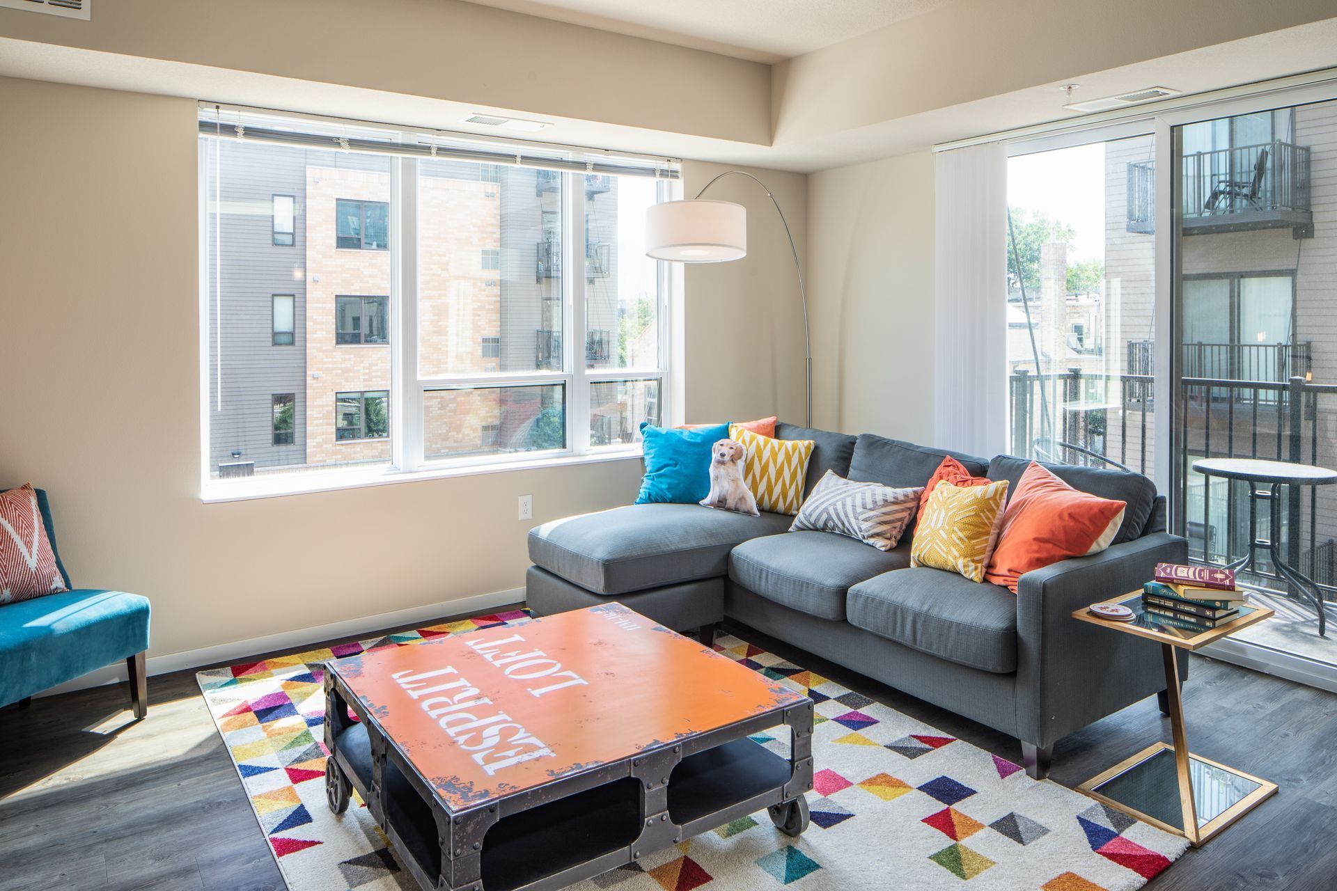 Living room with gray sectional sofa, colorful pillows, and a vibrant rug in a modern apartment.