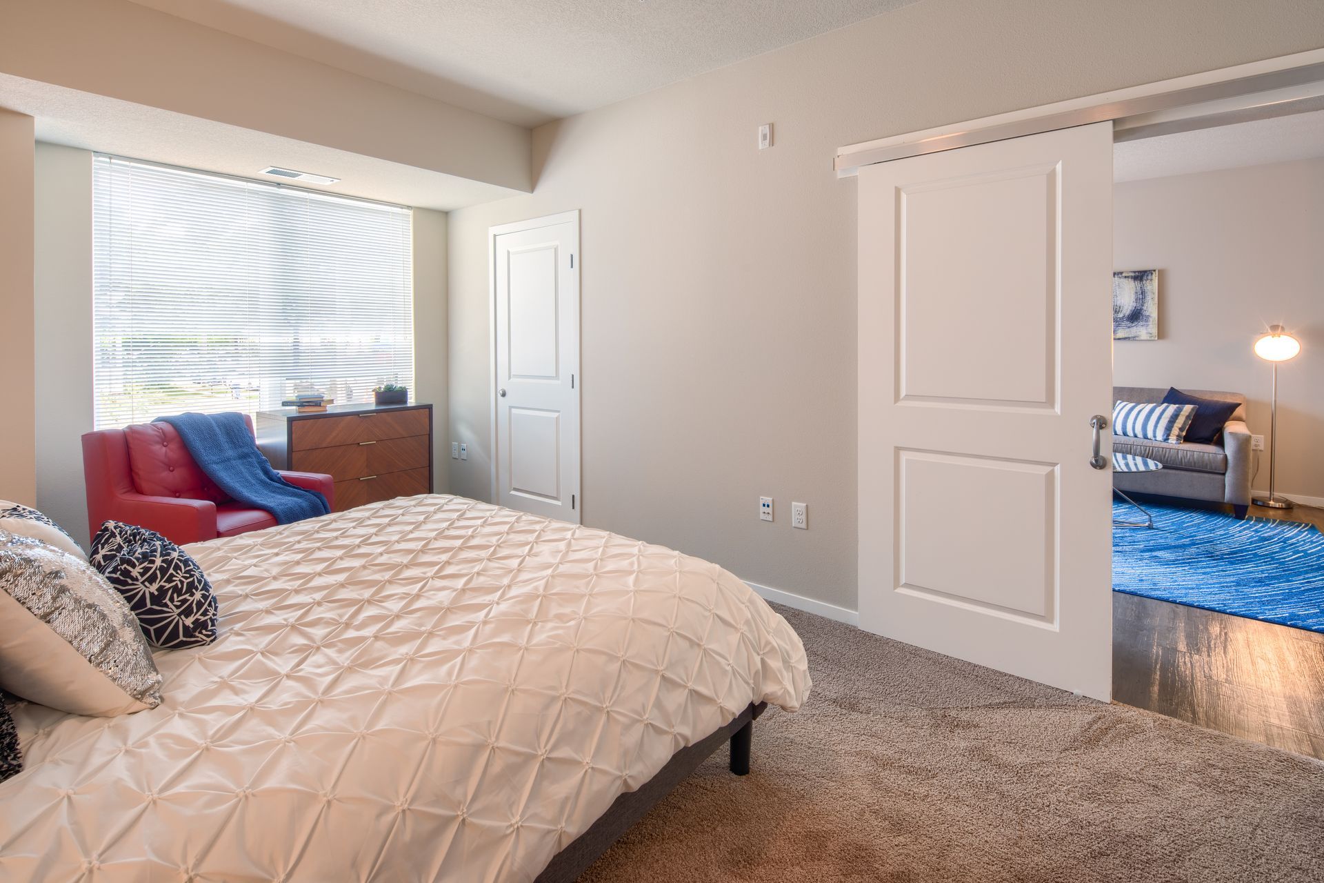 Bedroom with bed, red chair, dresser, and sliding door to living space with sofa.