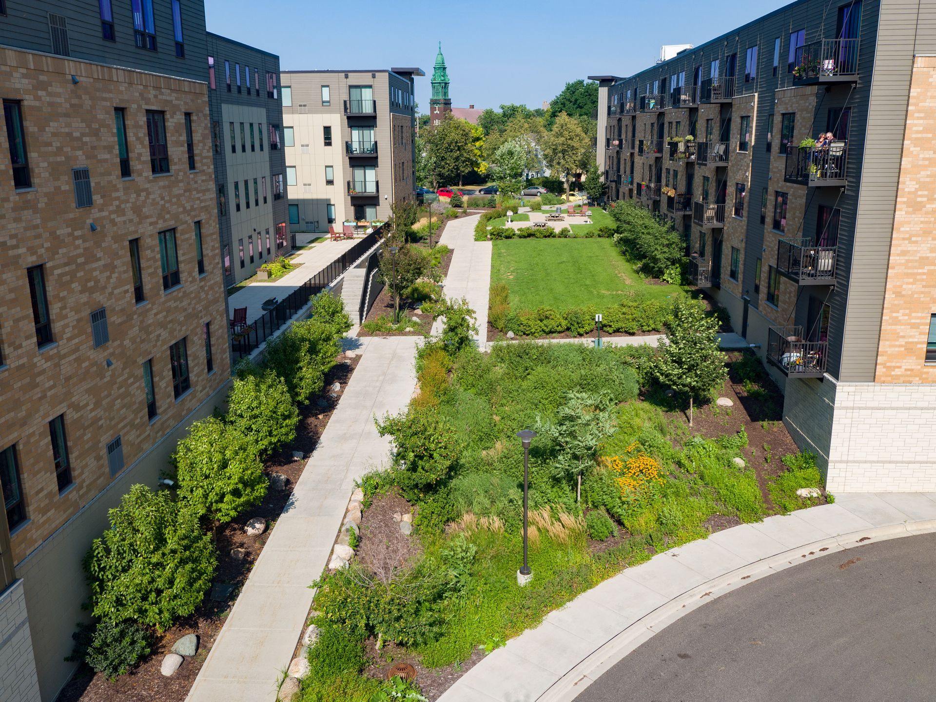A courtyard with walkways, green spaces, and apartment buildings on either side, under a blue sky.