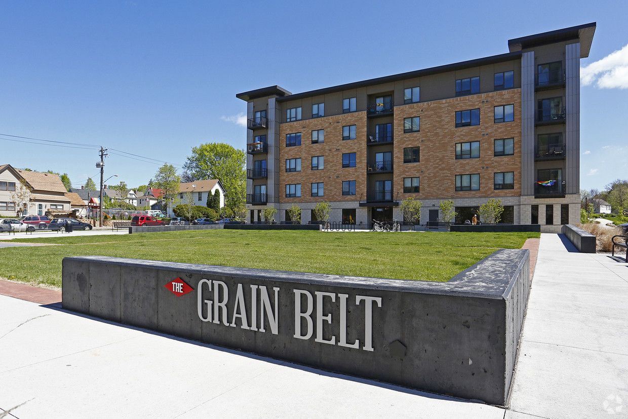 Grain Belt apartment building with a sign on a grassy area; sunny day.