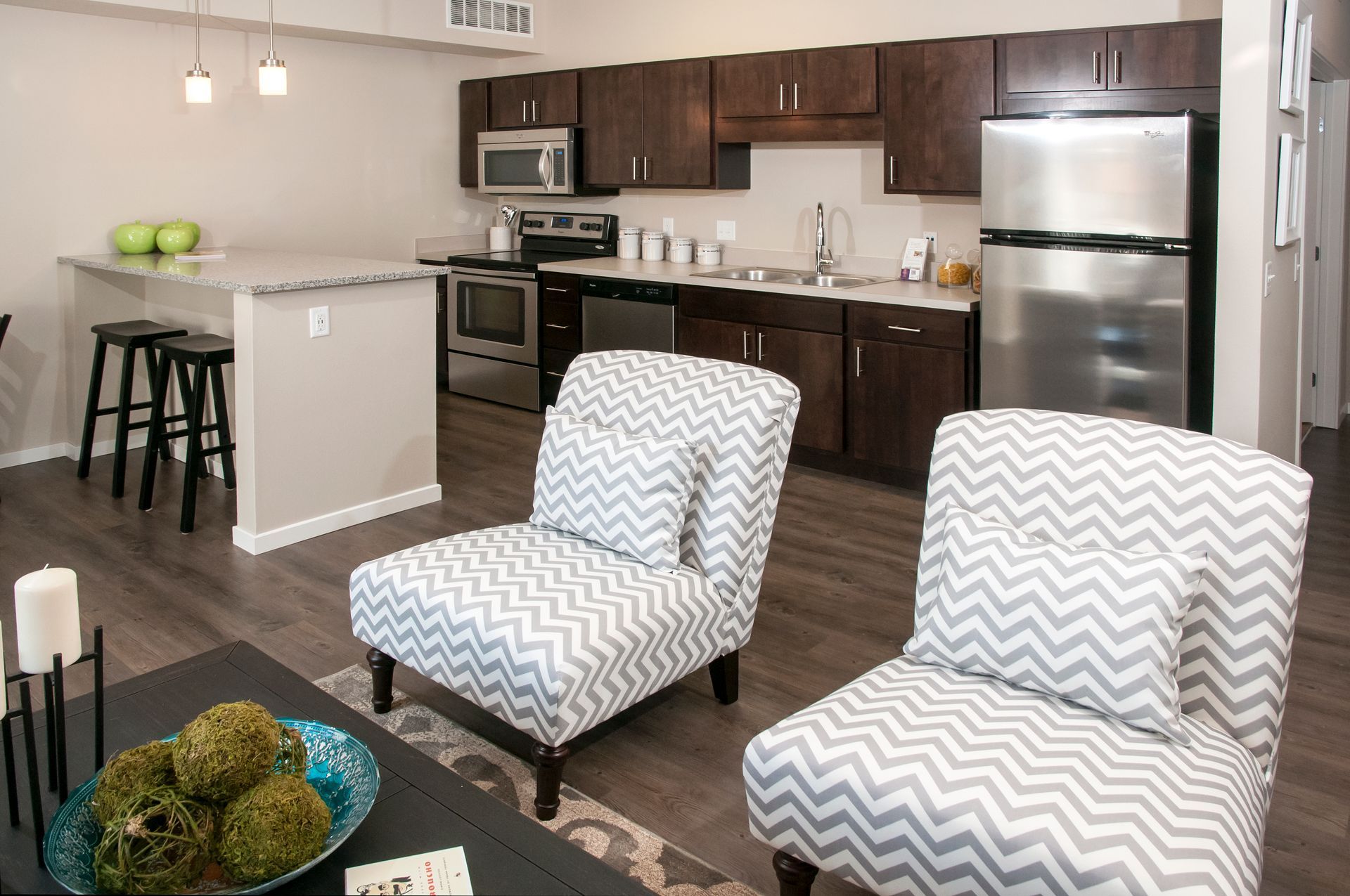 Living room and kitchen: Two patterned armchairs face a modern kitchen with stainless steel appliances.