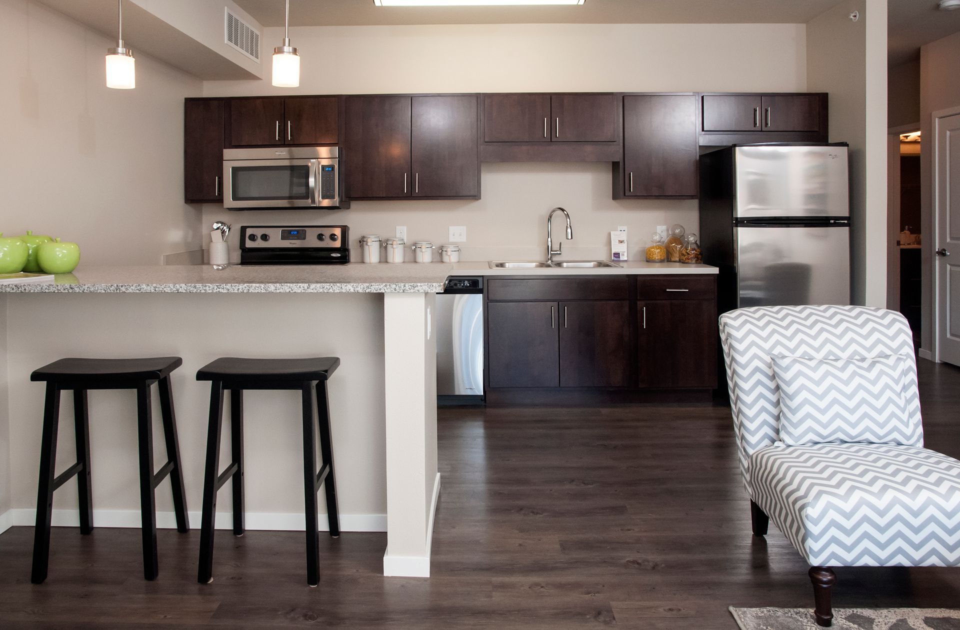 Kitchen with dark wood cabinets, stainless steel appliances, and a breakfast bar with two stools.
