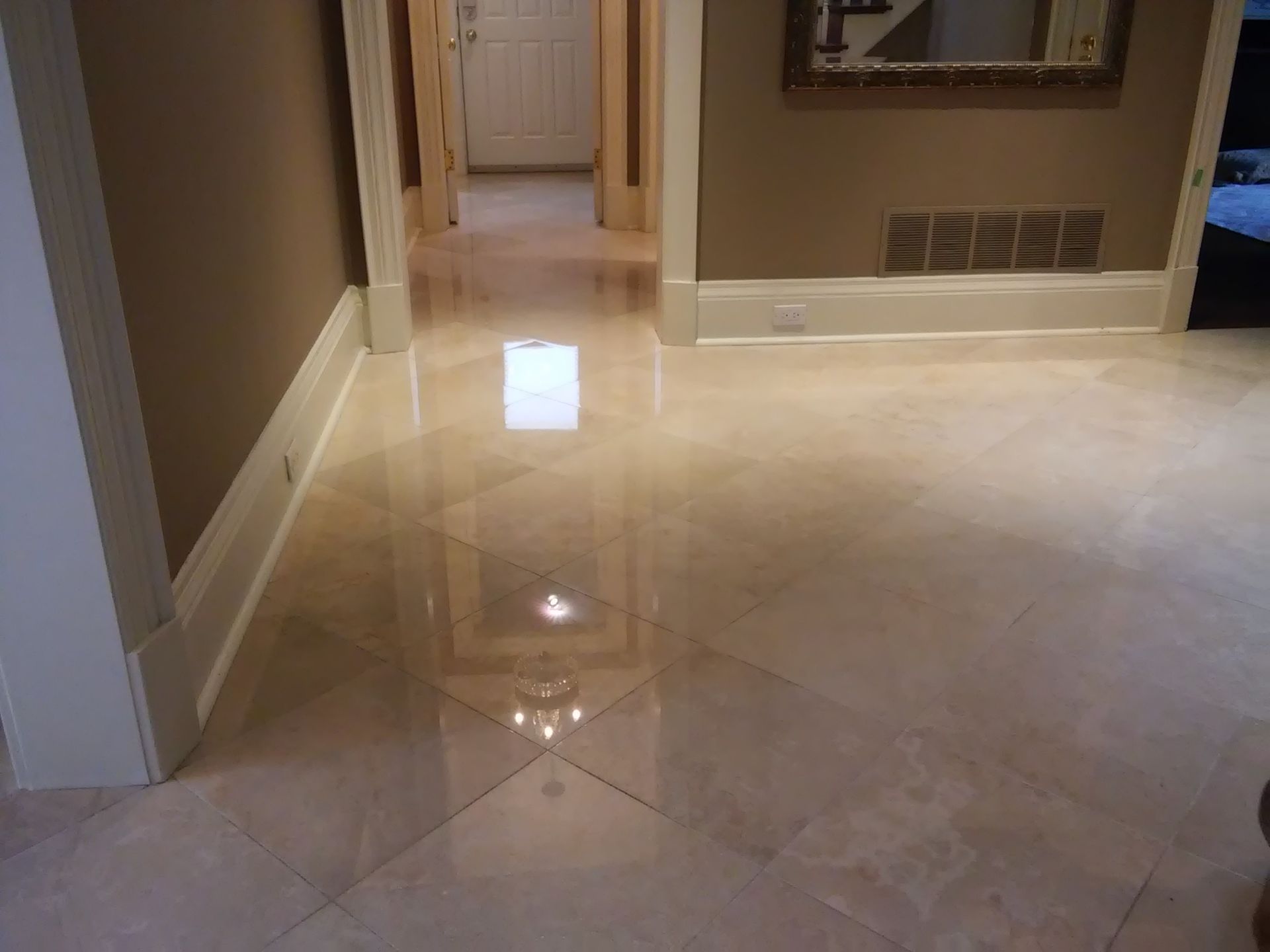 Shiny beige tiled hallway with doorway and wall vents in a home interior.