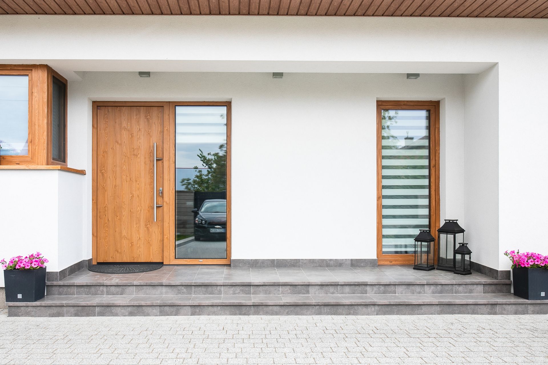 Modern house entrance with wooden doors, stone steps, and potted flowers