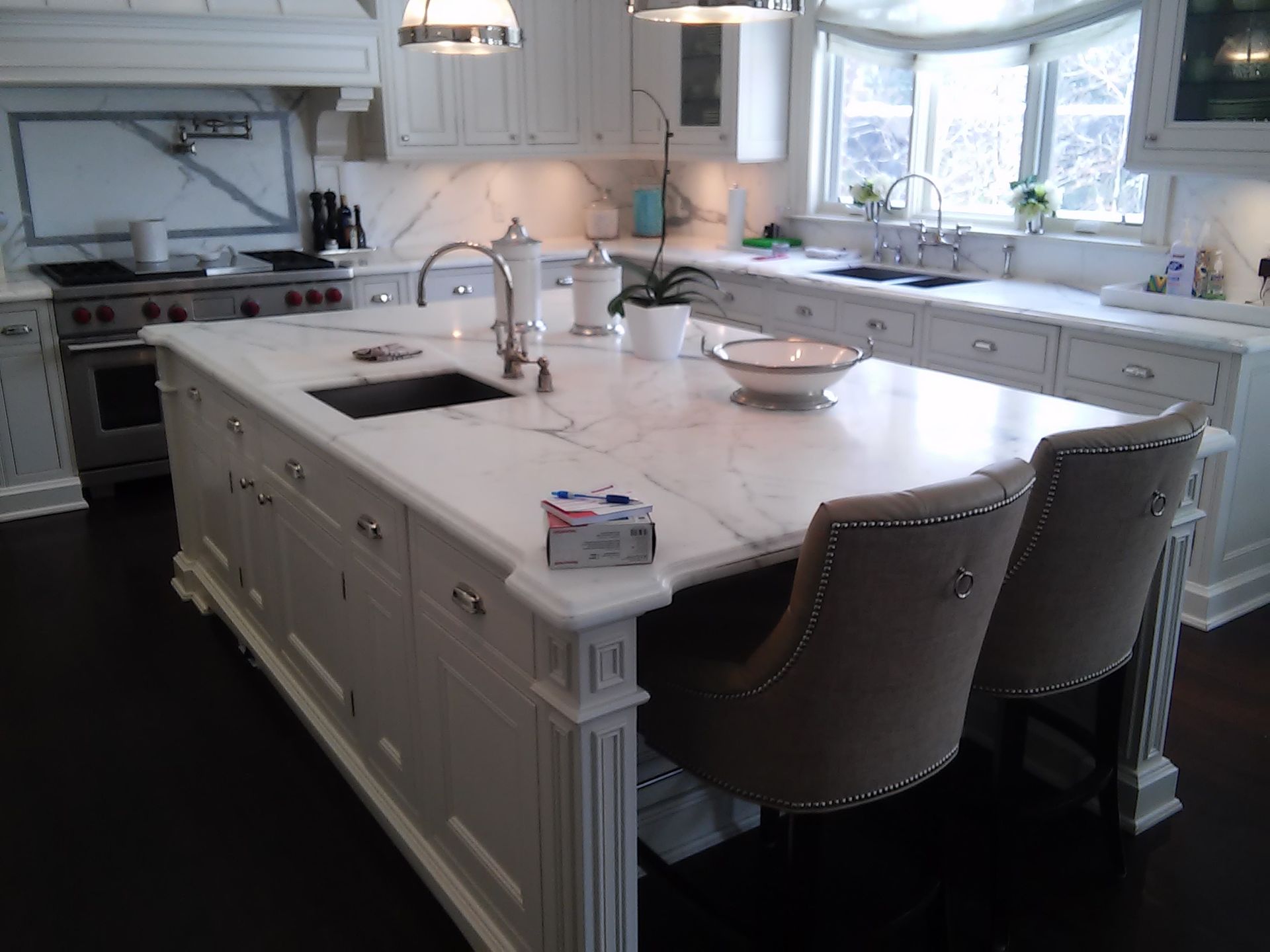 Bright white kitchen with a large island, stools, and a window above the sink