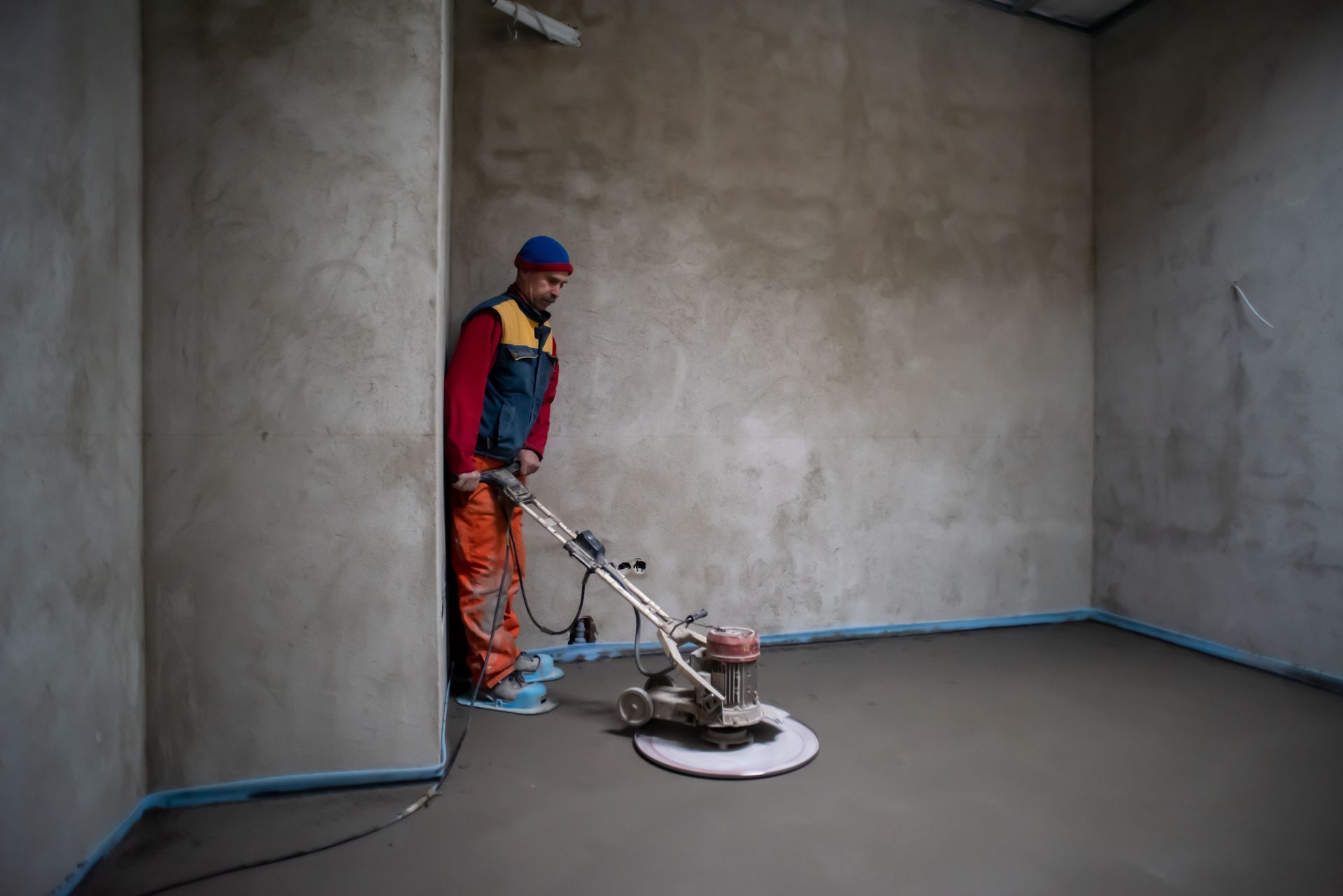 Worker using a floor polisher on a smooth gray floor in an unfinished room