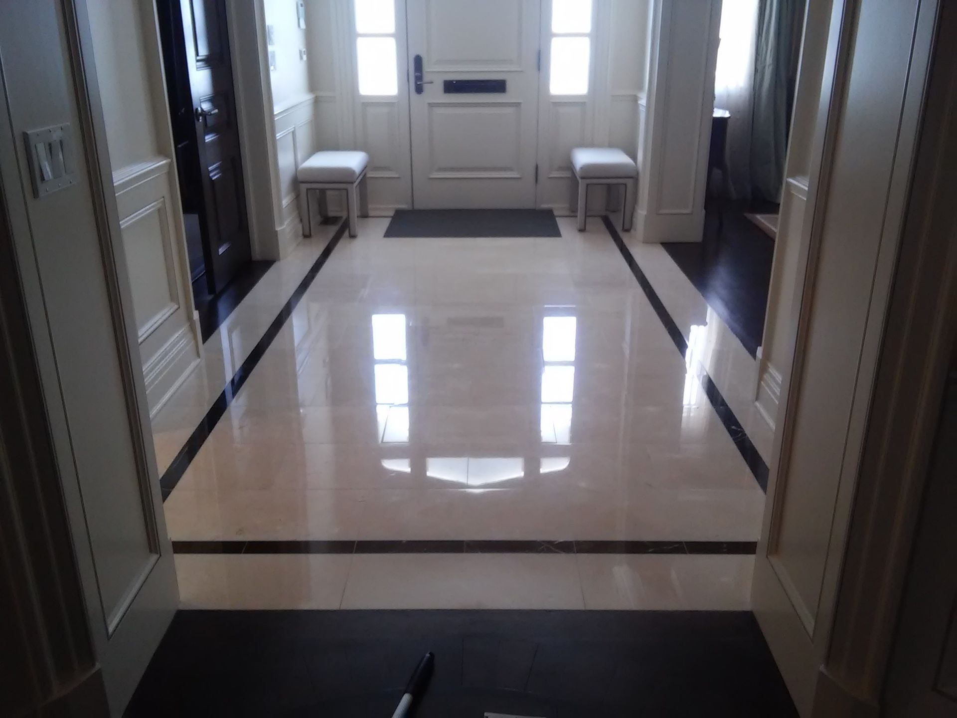 Bright hallway with polished marble floor, white walls, and benches by a front door.