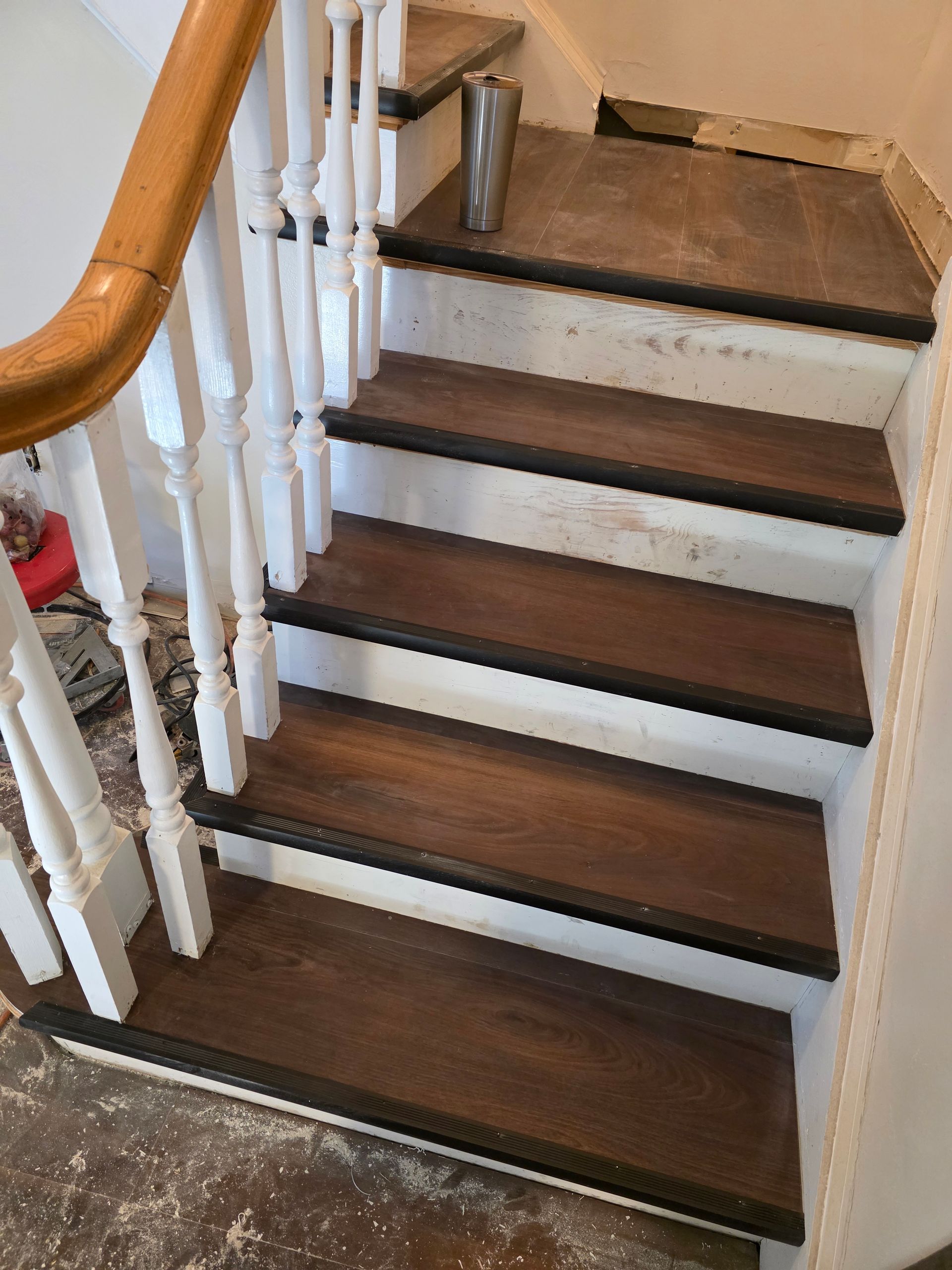 Indoor staircase with dark wood steps, white balusters, and a wooden handrail, viewed from the bottom.