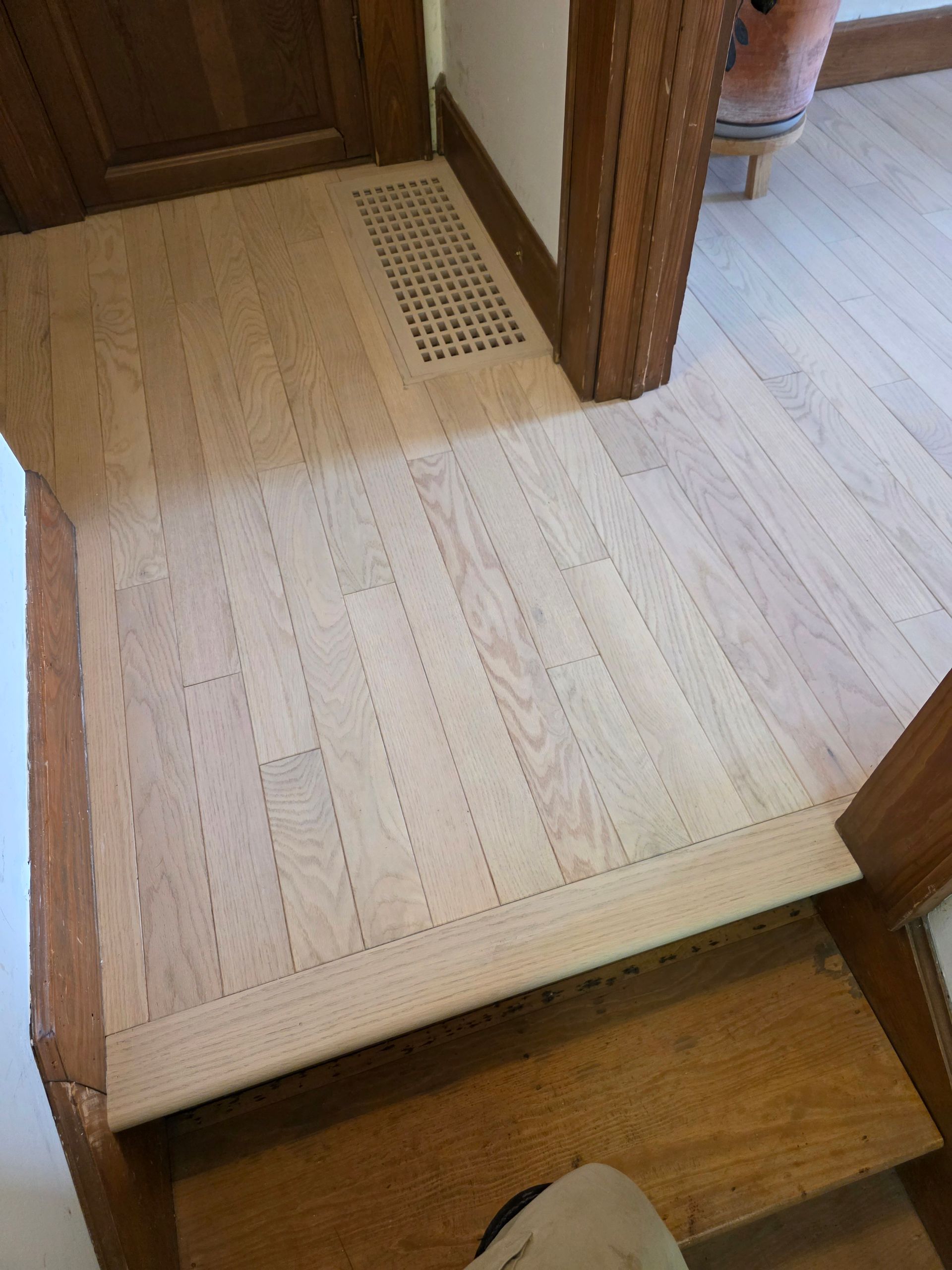 Wooden hallway floor with a raised threshold and vented floor register near a doorway.