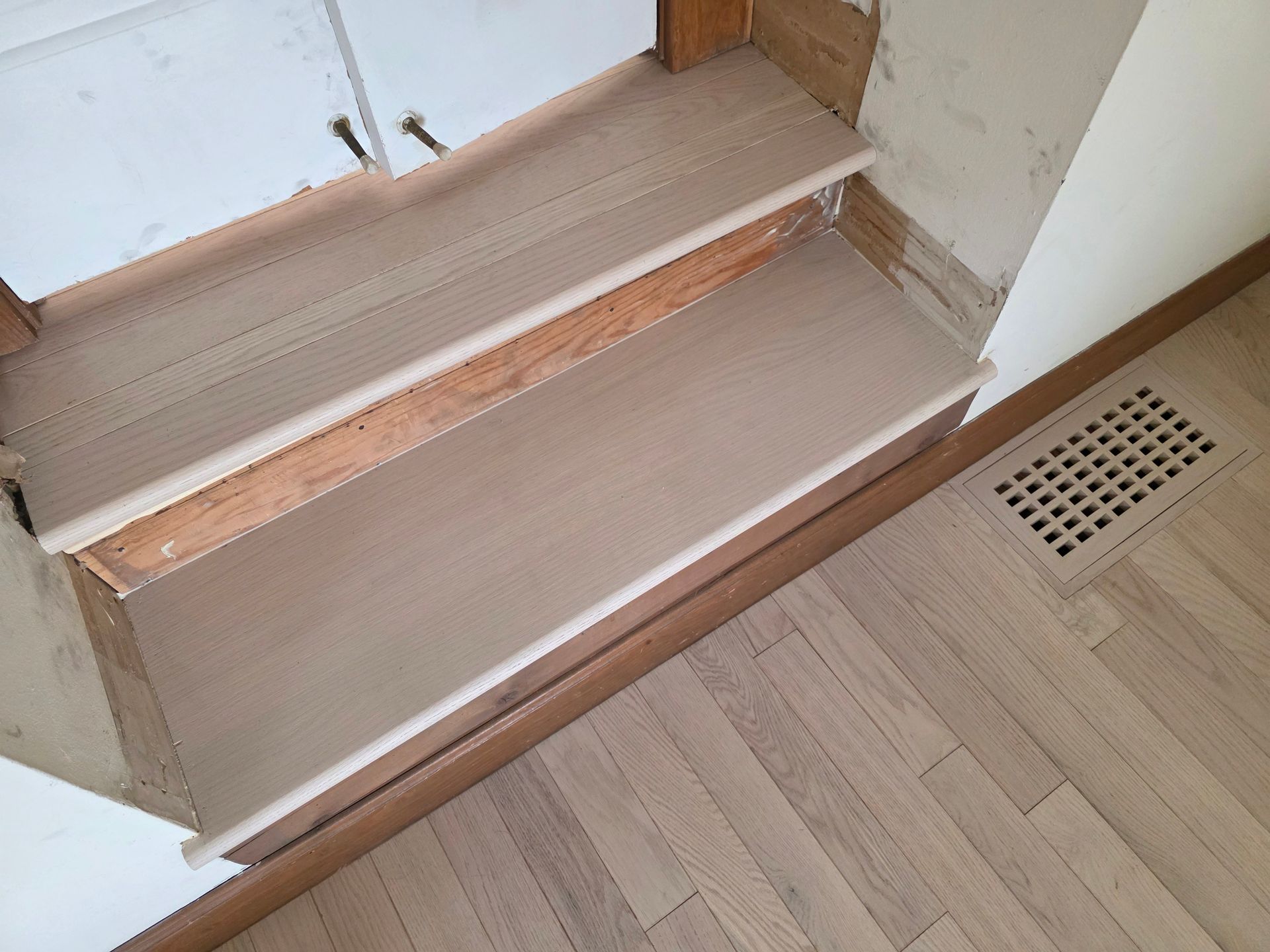 Indoor stairway with a beige carpeted step and a small floor vent beside it