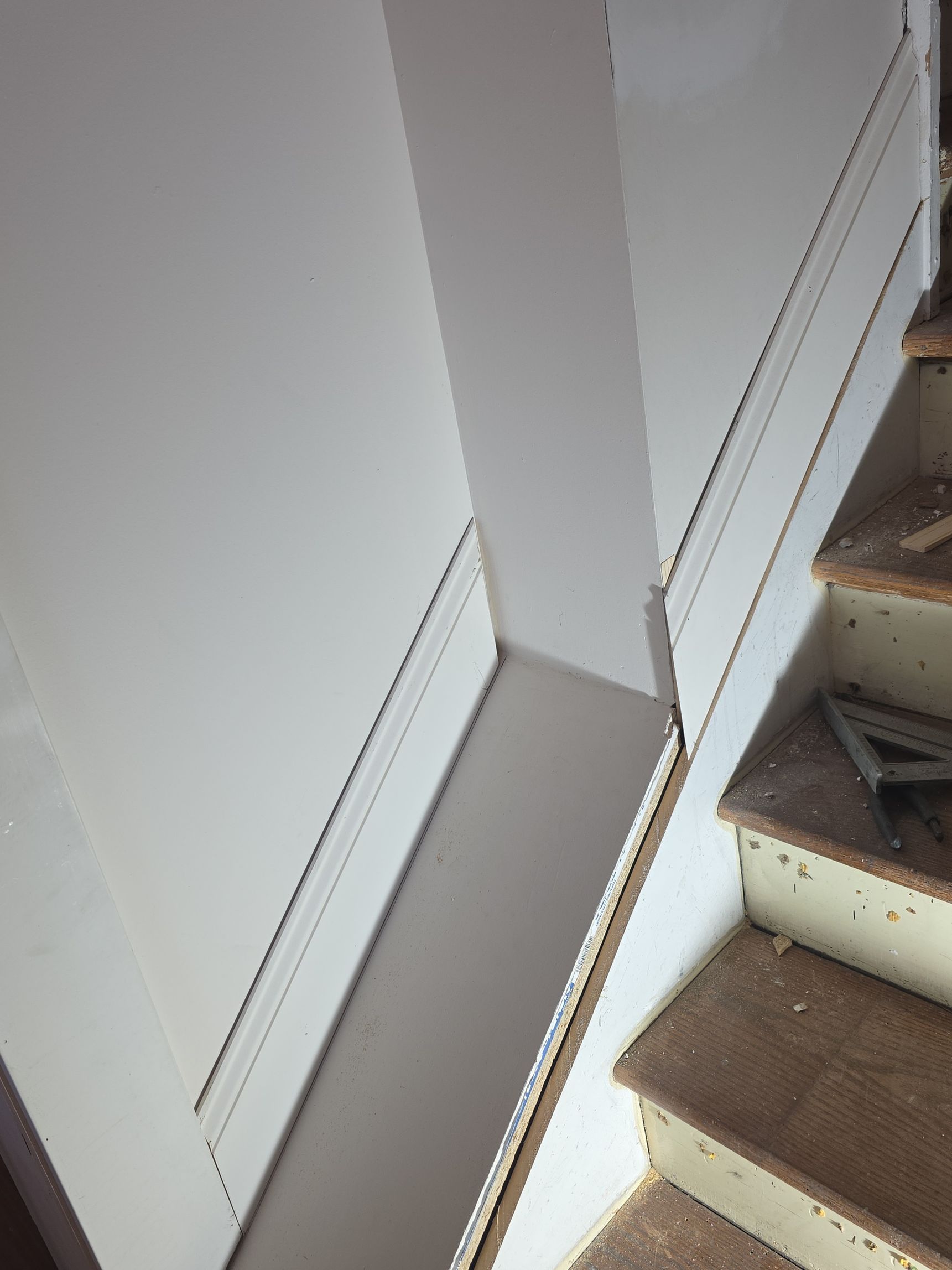 Narrow stairwell beside a white wall, with carpeted steps and a small landing.