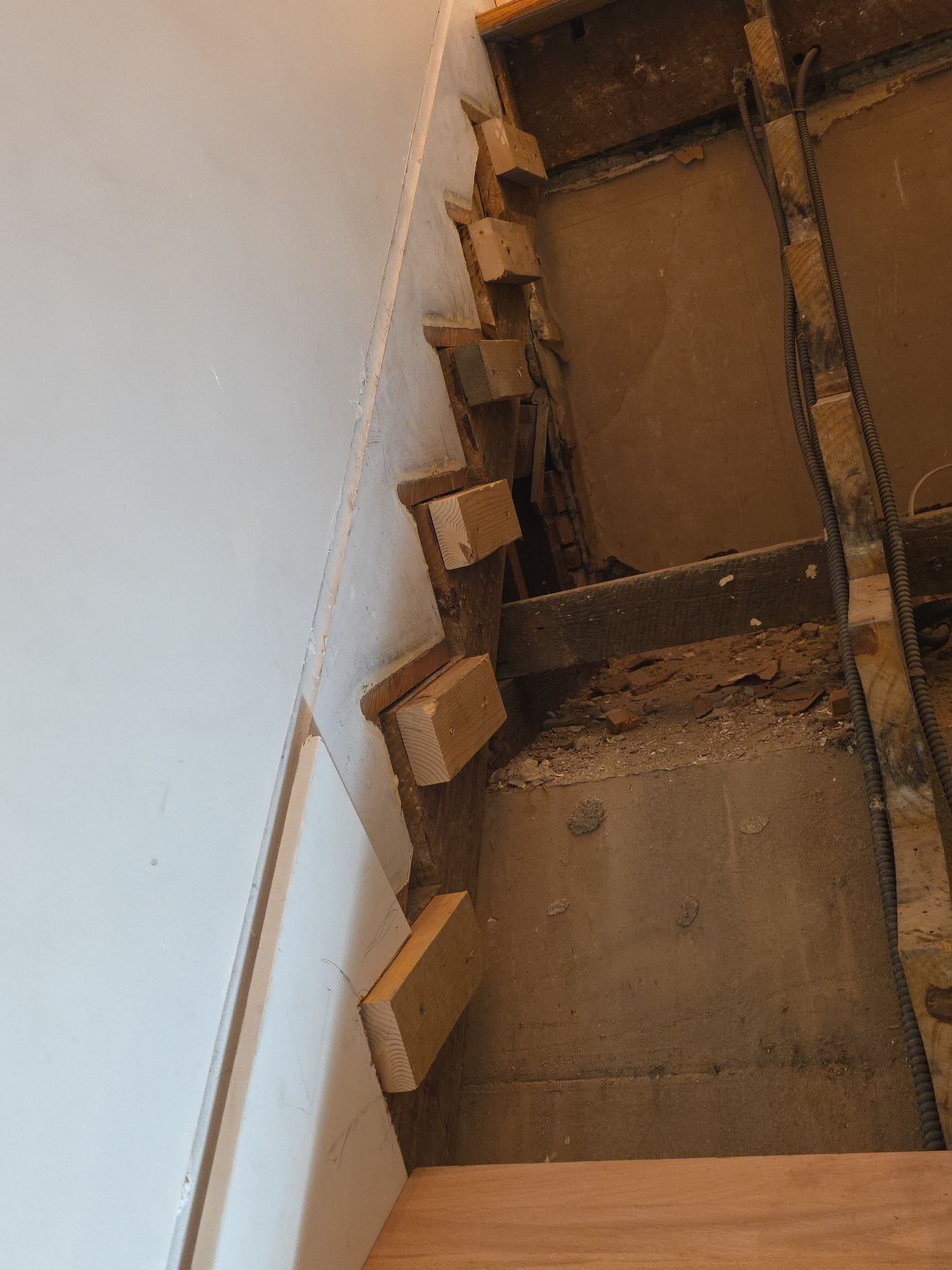 Steep indoor stairwell under construction, with rough wooden steps and debris on the landing.