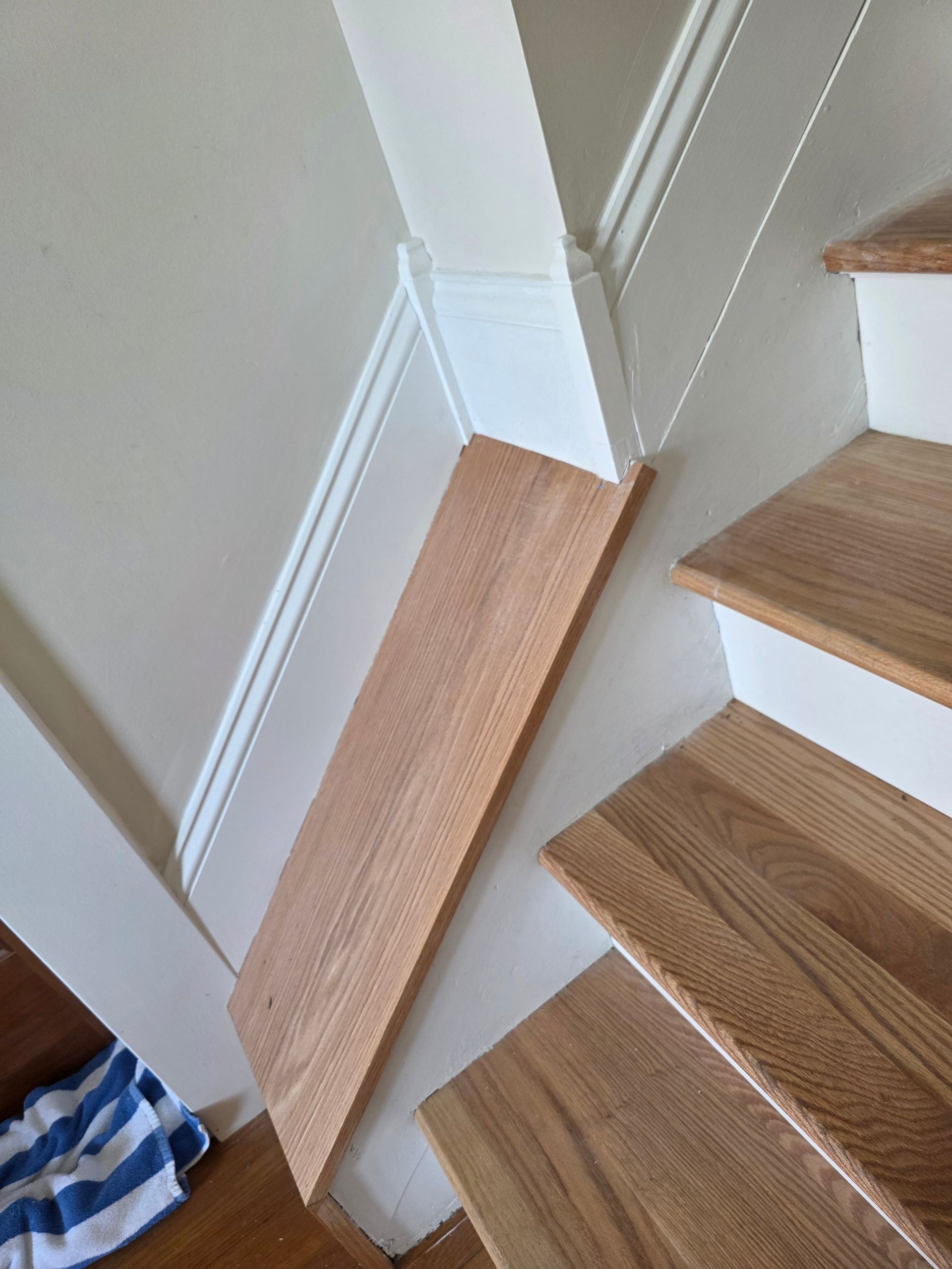 Wooden stairlift rail beside carpeted stairs in a narrow hallway