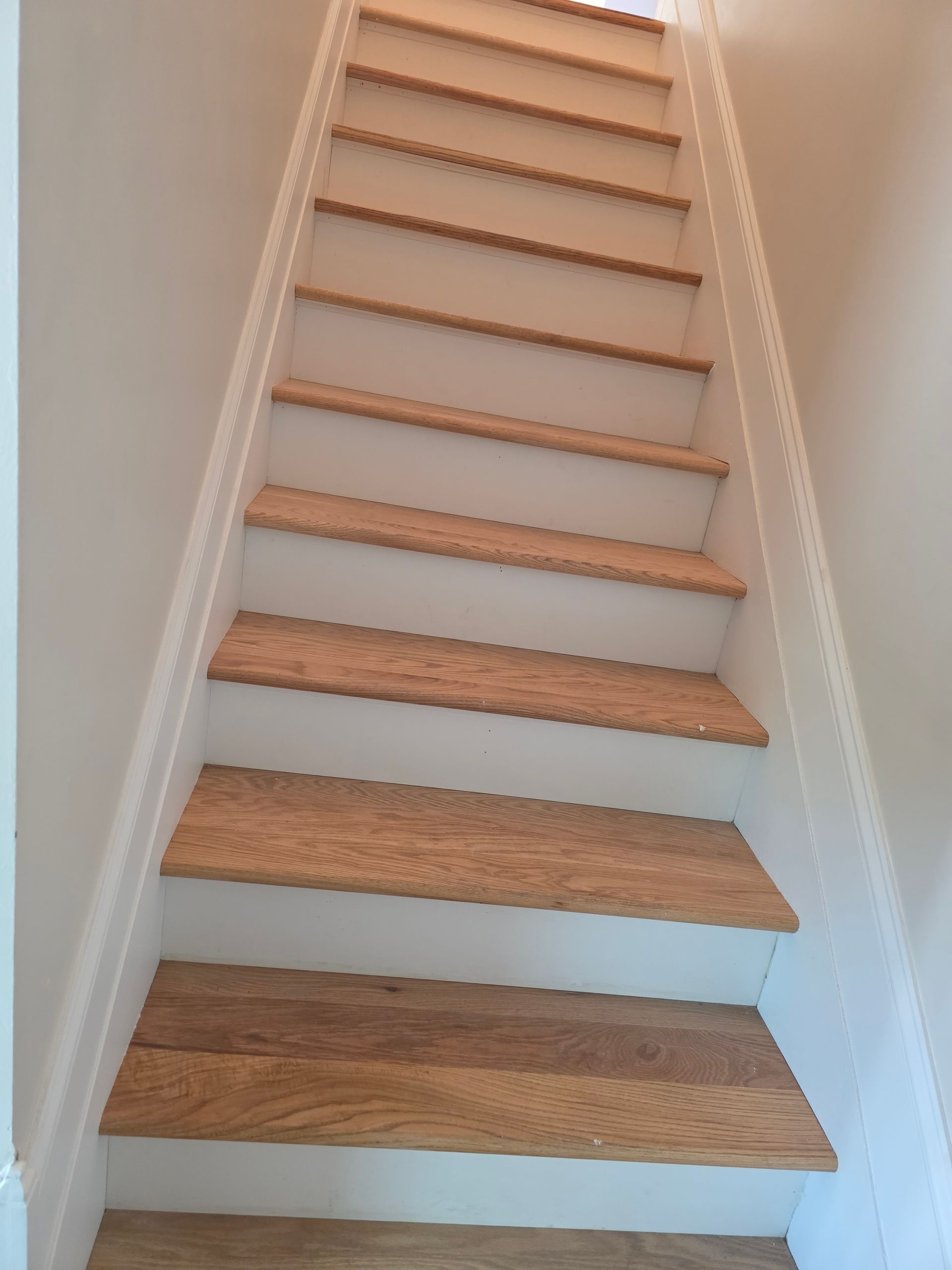 Wooden staircase with beige walls, viewed from below.