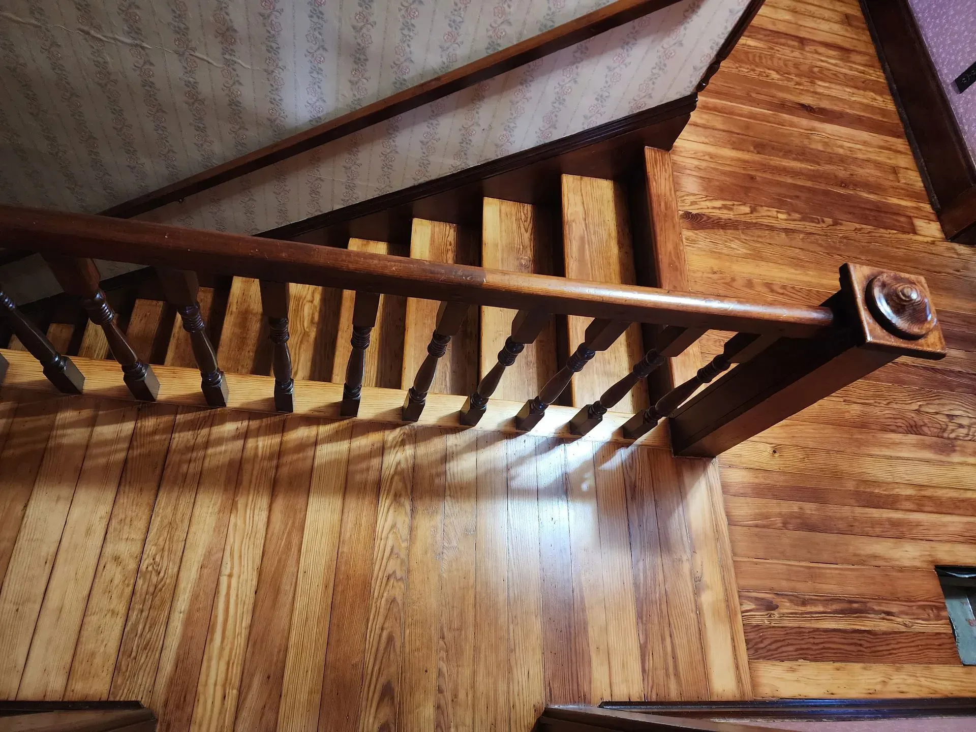 Wooden staircase with open balusters and warm brown wood paneling in a rustic interior.