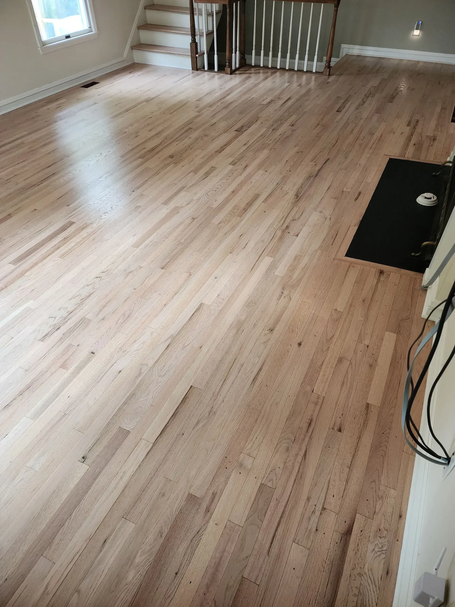Empty room with light wood floors, white walls, and a small black mat near a stair railing.