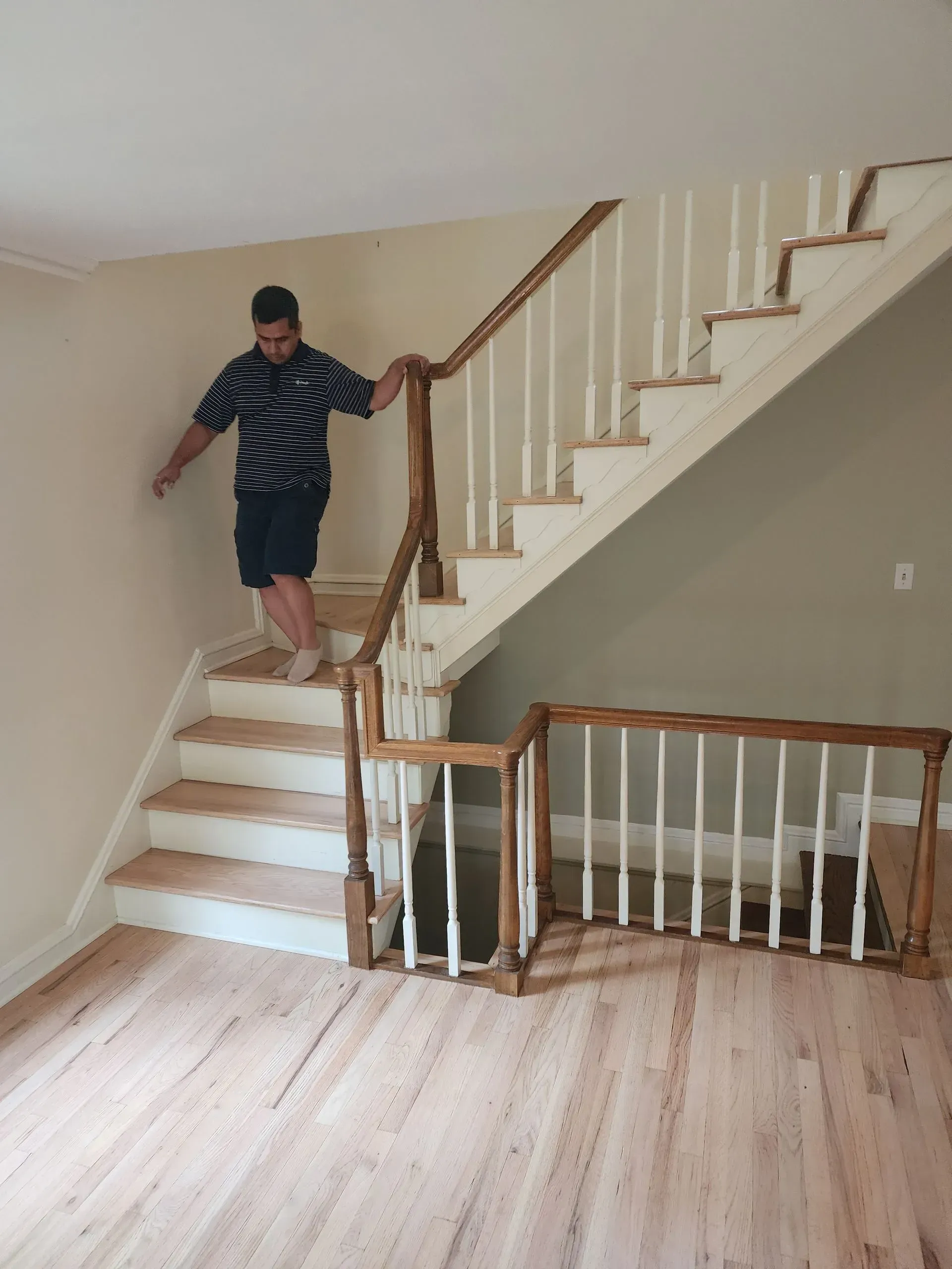 Person descending a white wooden staircase in a beige room with a hardwood floor.