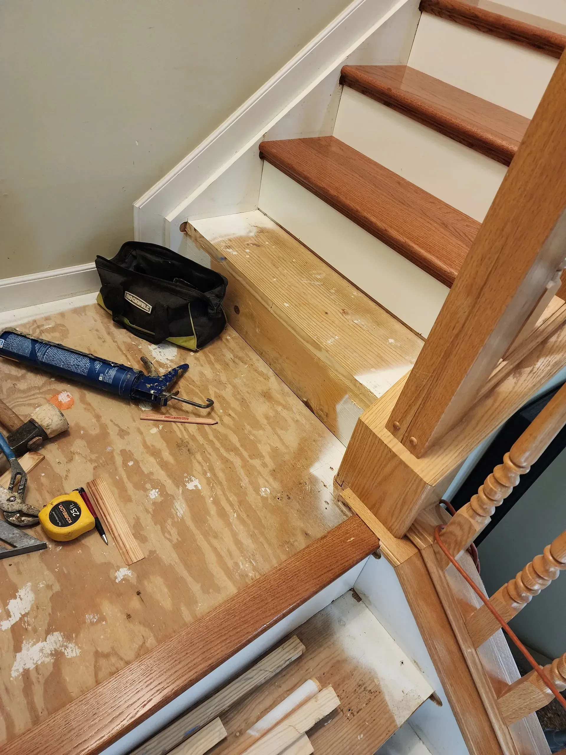 Stairway under repair with tools, plastic sheeting, and exposed plywood steps.