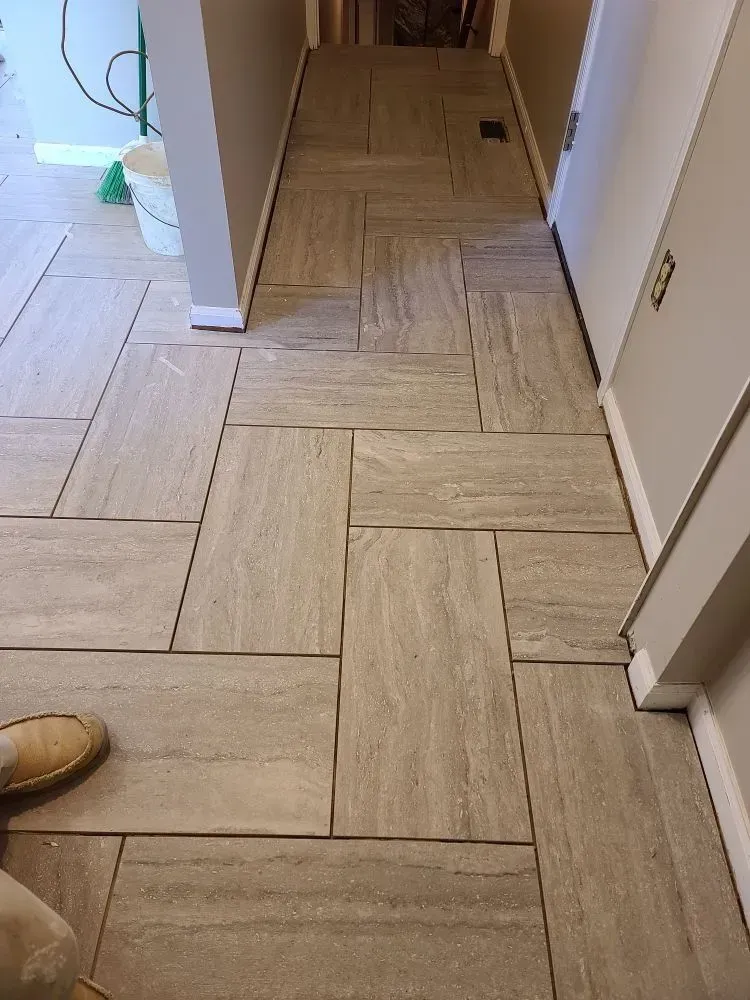 Narrow hallway with light wood herringbone flooring and white walls, viewed toward a doorway.
