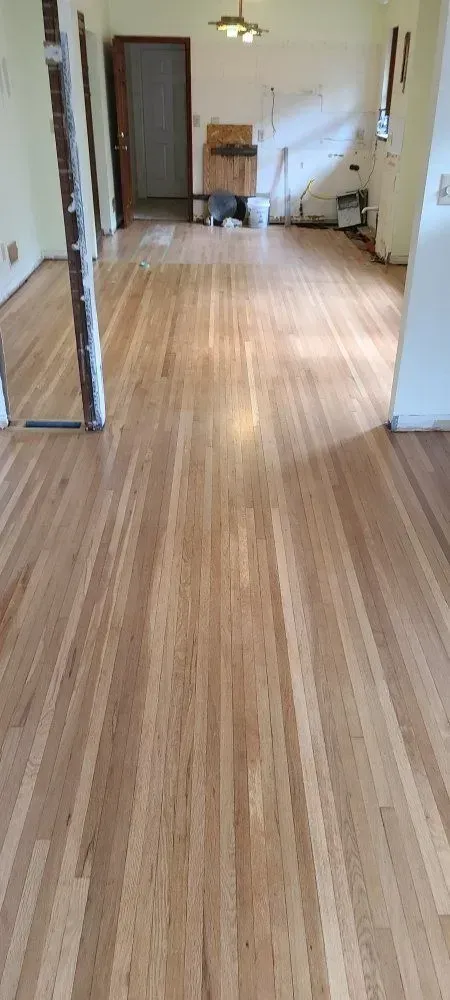 Empty hallway with wood flooring, open doors, and a small chair in the distance.