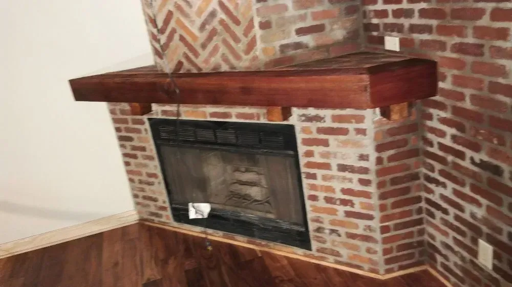 Brick fireplace with dark wood mantel and hearth in a room with wood flooring.