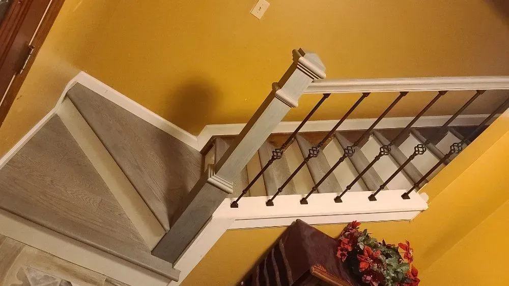 Staircase with white railing and beige carpeted steps against a yellow wall, viewed from above.