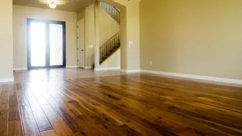 Empty living room with hardwood floors, beige walls, staircase, and sliding glass doors letting in light