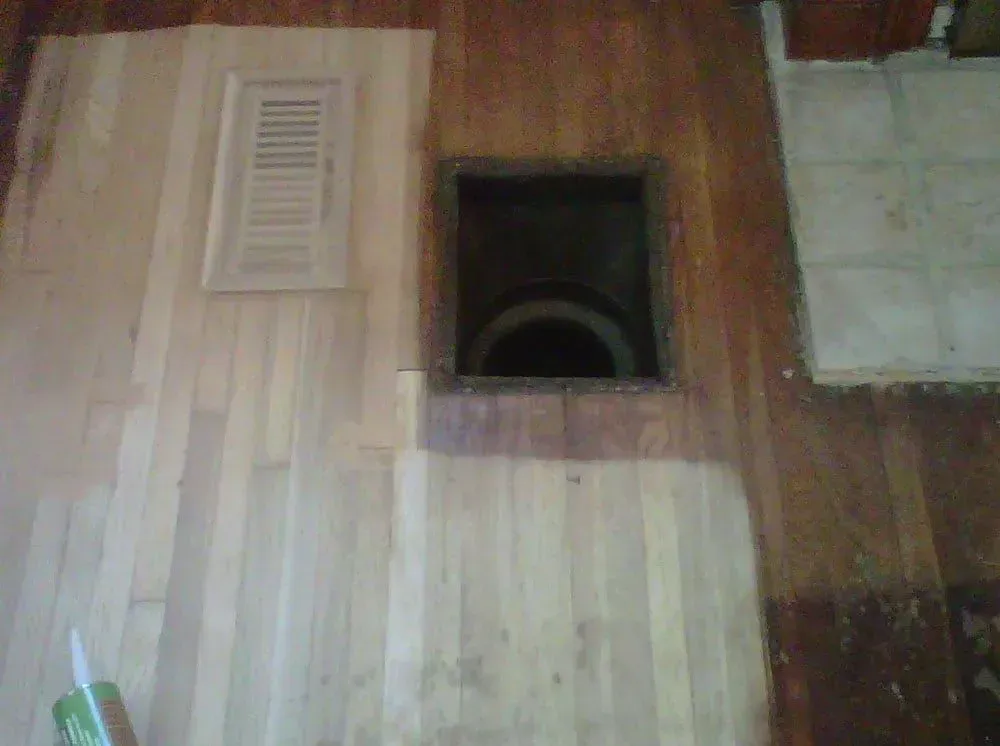 Wooden floor with a square cutout opening and a vent cover nearby